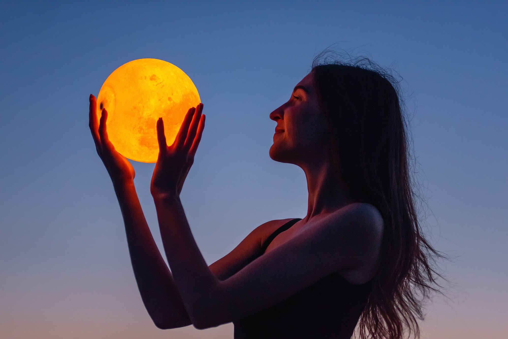 A young woman holds the full moon in her hands against the backd